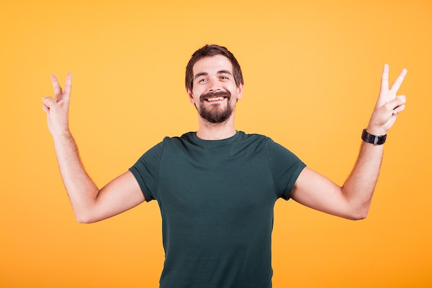 Happy smiling man showing victory peace sign with both hands isoalted on yellow background in studio