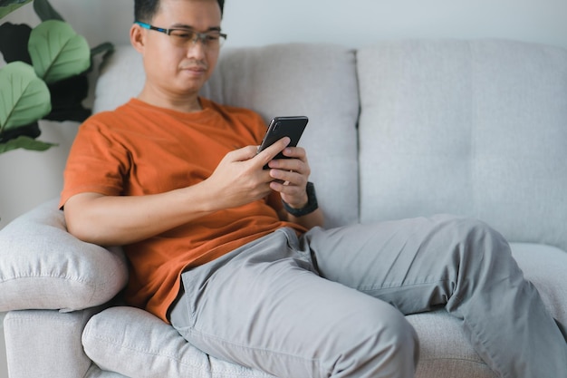 Happy smiling man using smartphone device while chilling on sofa a home cheerful hipster guy typing an sms message