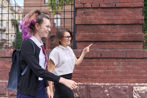 Happy smiling mother and daughter teenager student walking and talking together outdoor, copy space