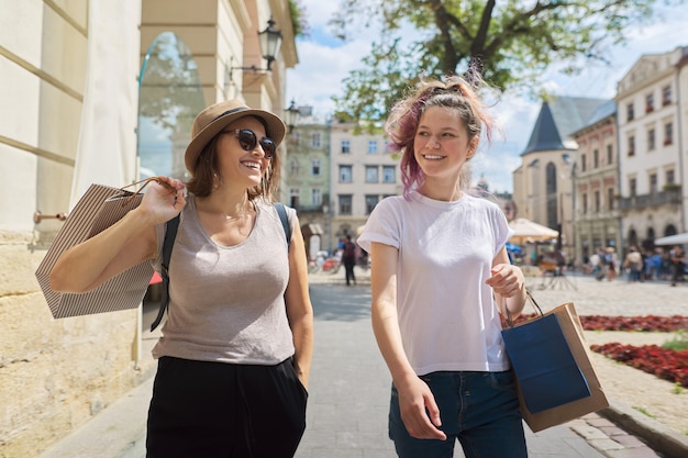 Happy smiling mother and teenage daughter walking together with shopping bags