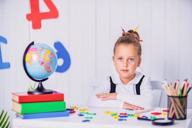 Happy smiling pupil at the desk. Child in the class room with pencils, books. Kid girl from primary school.