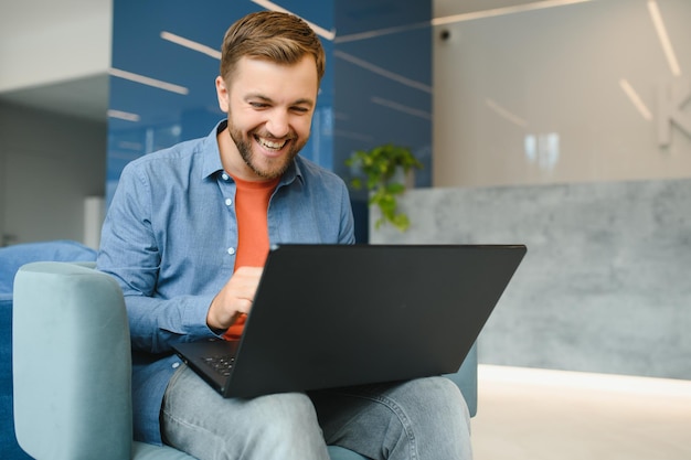 Happy smiling remote online working man in casual outfit with laptop in joyful successful winning gesture sitting in an coworking office at a work desk