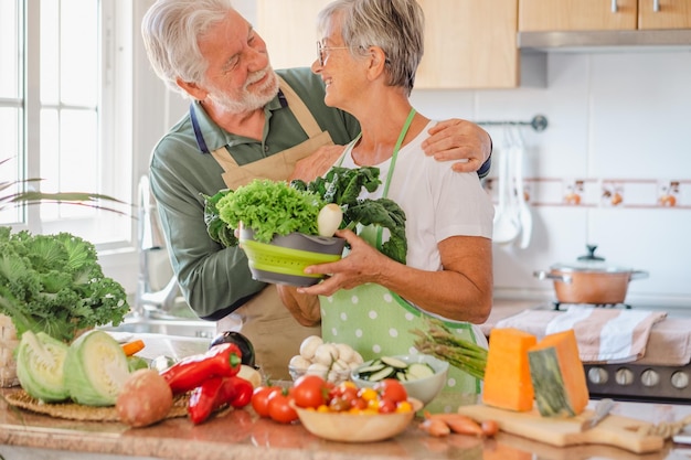 Happy smiling senior couple working together in home kitchen preparing vegetables enjoying healthy eating veganism or vegetarian concept