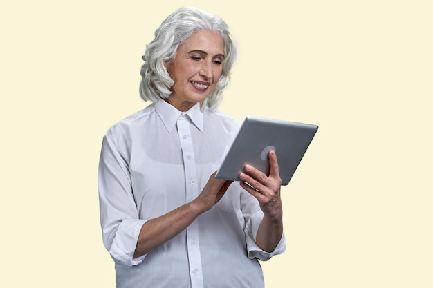 Happy smiling senior woman with tablet pc isolated on pastel yellow background