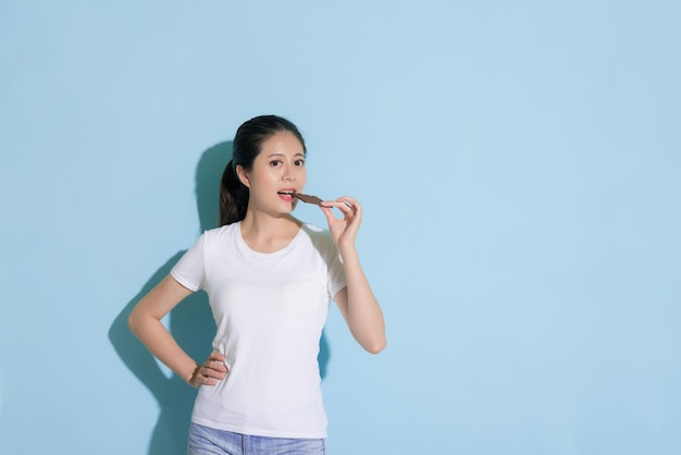 happy smiling woman eating delicious chocolate food looking at camera and standing in blue background enjoying dessert time.