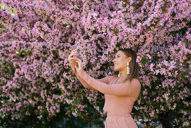 A happy smiling woman takes a selfie on her smartphone in a spring blooming garden enjoying nature