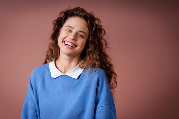 Happy smiling young adult woman wearing winter blue sweater indoors looking at camera with joyful smile