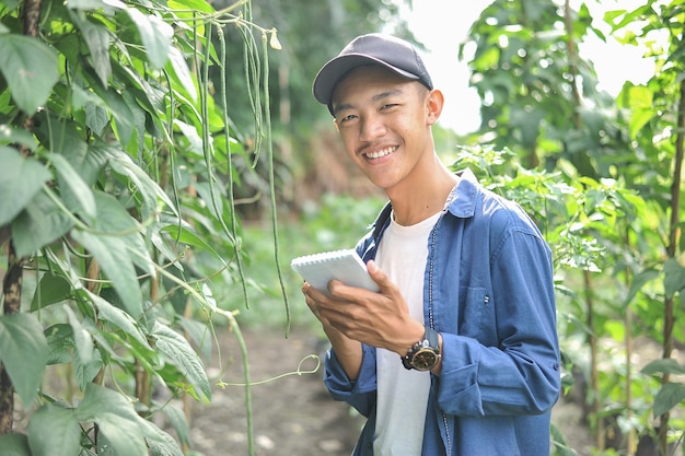 Happy of smiling young Asian farmer male holding the notebook on green garden, on location.