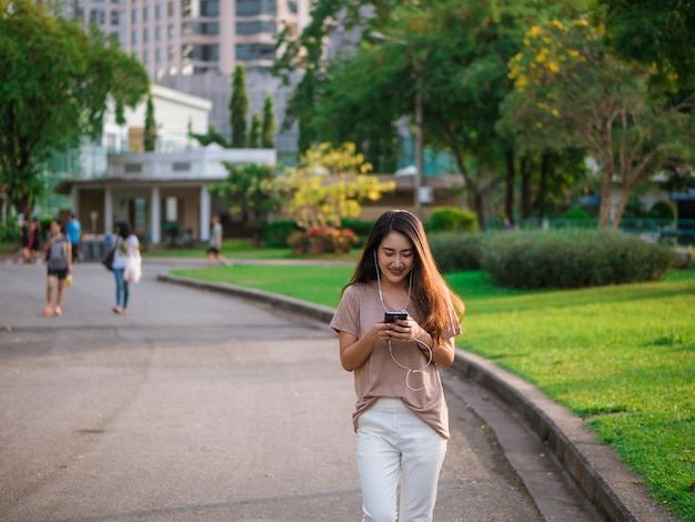 Happy smiling young asian woman listens to music in headphone and using smartphone.