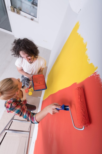 happy smiling young couple painting interior wall of new house