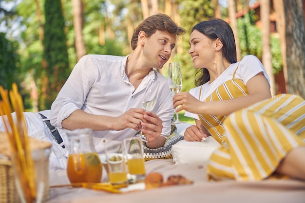 happy smiling young couple sitting in the garden and drinking cold champagne