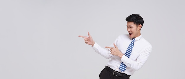 happy smiling young handsome Asian businessman pointing away and looking isolated on white