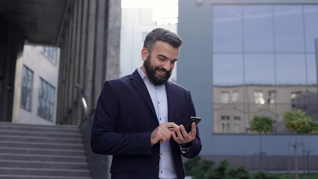 Happy smiling young man using mobile phone apps, texting message, browsing internet, watching video,tapping,looking at smartphone