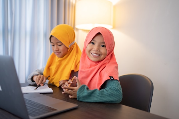 Happy smiling young muslim kid with laptop together looking at camera