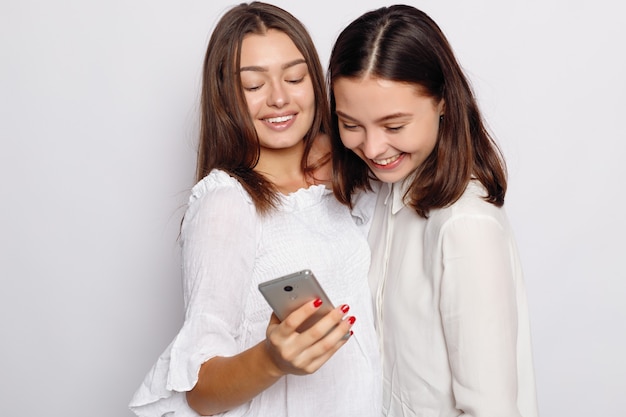 Happy smiling young woman showing photos on mobile phone to her friend.