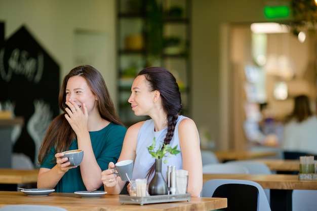 Happy smiling young women with coffee cups at cafe. Communication and friendship concept