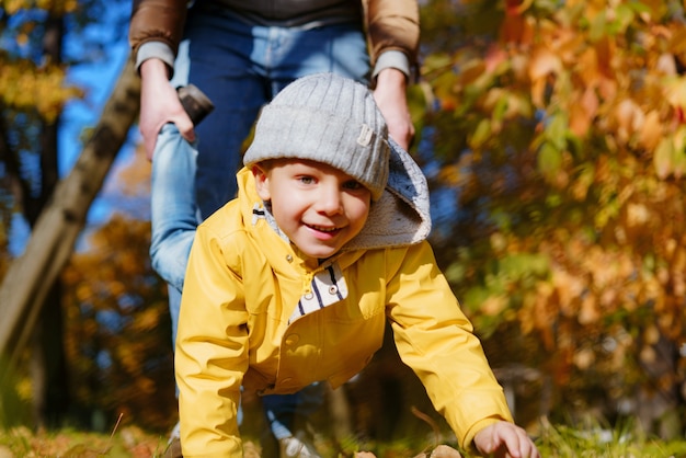 Happy smilingboy in yellow jacket having fun walking on his hands Father holding him by feet