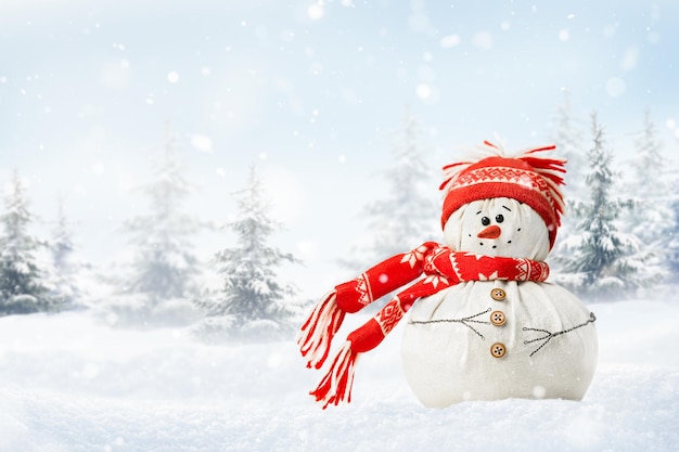 Happy snowman in a snowdrift in a red hat and scarf against the backdrop of a winter forest