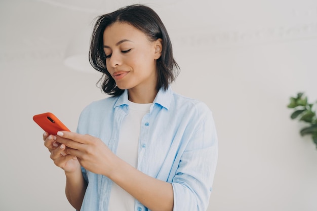 Happy spanish woman is texting on smartphone and smiling SMS messages reading and typing