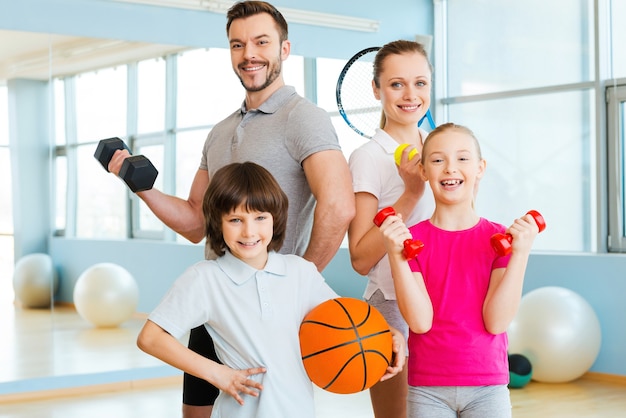 Happy and sporty. Happy family holding different sports equipment while standing close to each other in health club