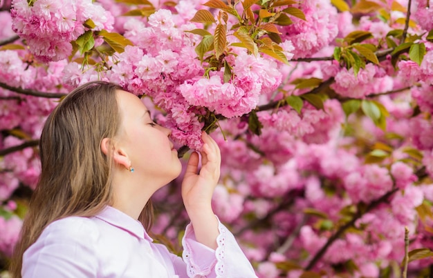 Happy spring vacation. Spring in botany garden. That is how spring smells. Tender bloom. Little girl enjoy spring. Kid on pink flowers of sakura tree background. Kid enjoying cherry blossom sakura.