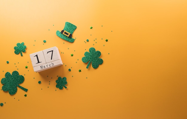 Happy St Patrick's Day decoration concept made from shamrocks clover leaf wooden calendar and leprechaun hat on yellow background