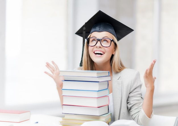 happy student in graduation cap with stack of books