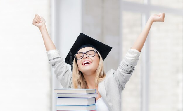 Photo happy student in graduation cap with stack of books