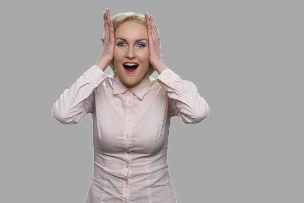 Happy stunned woman looking at camera. Portrait of excited shocked business woman holding hands on head.