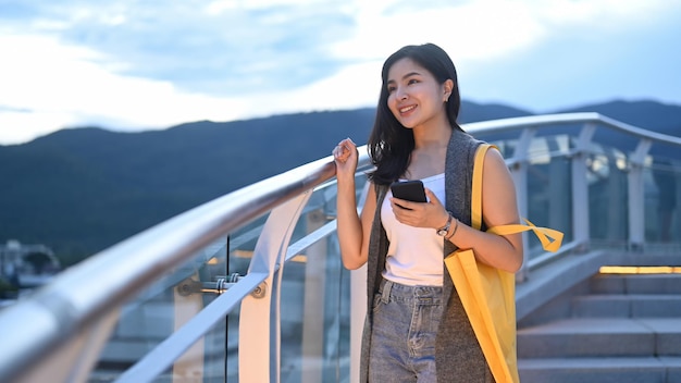 Happy stylish asian woman standing on rooftop terrace with beautiful nature view in evening