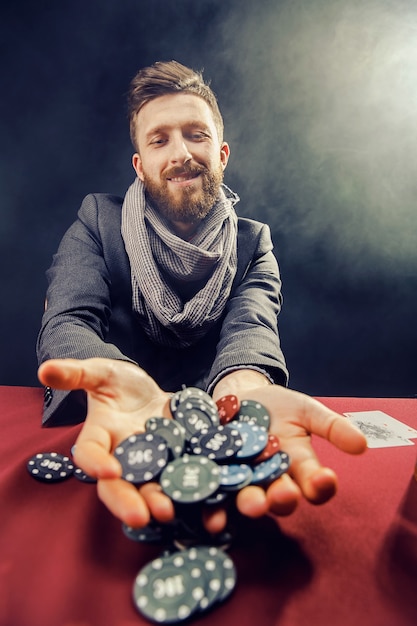 Happy stylish bearded man in suit and scarf playing in dark casino