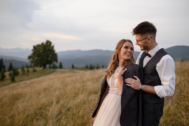 Happy stylish bride and groom running and having fun in mountains on summer sunny day