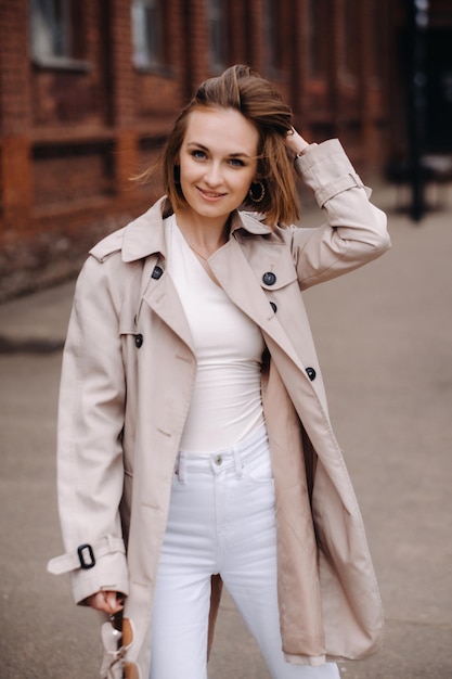 A happy stylish girl in a gray coat walks around the city