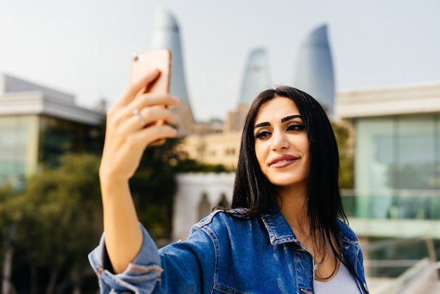 Happy stylish woman doing selfie on city background