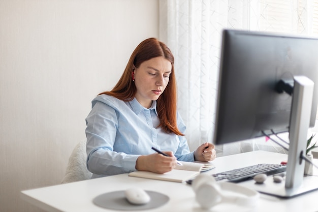 Happy stylish woman remote working from home distance office on pc taking notes smiling