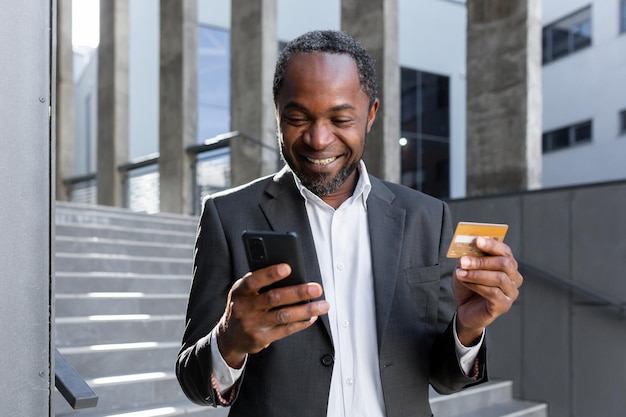 Happy and successful african american man in business suit outside office building holding bank