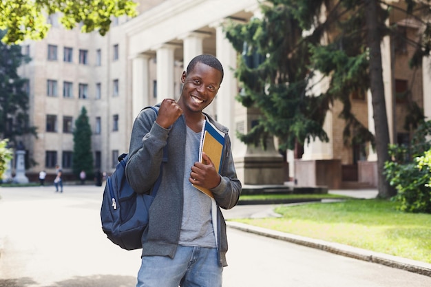 Happy successful african-american student with books, celebrating victory outdoors. Education, winner and achievement concept, copy space