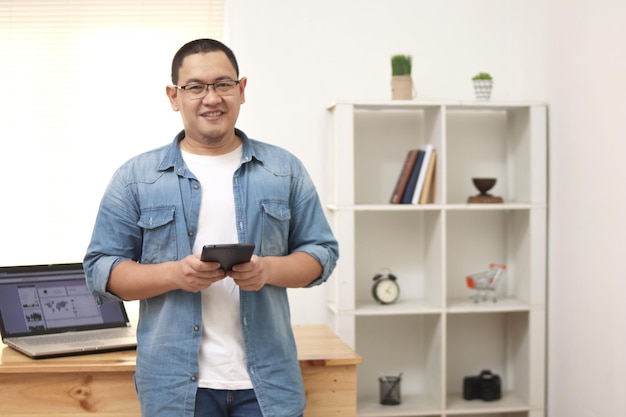 Happy successful Asian male holds tablet checking his online business freelancer internet concept