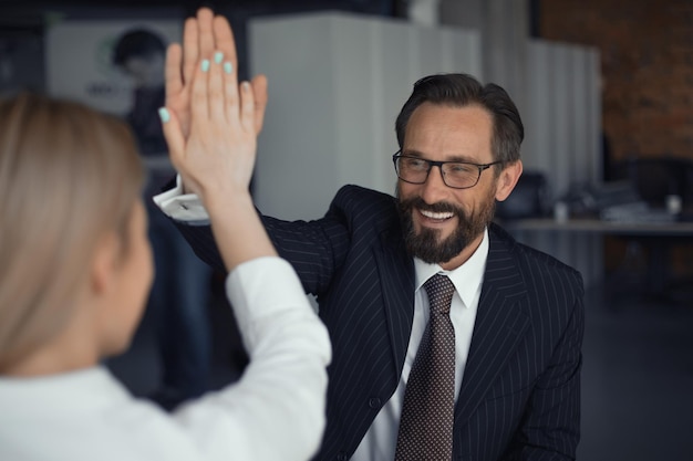 Happy successful businessman giving high five with businesswoman standing back in foreground teamwor...