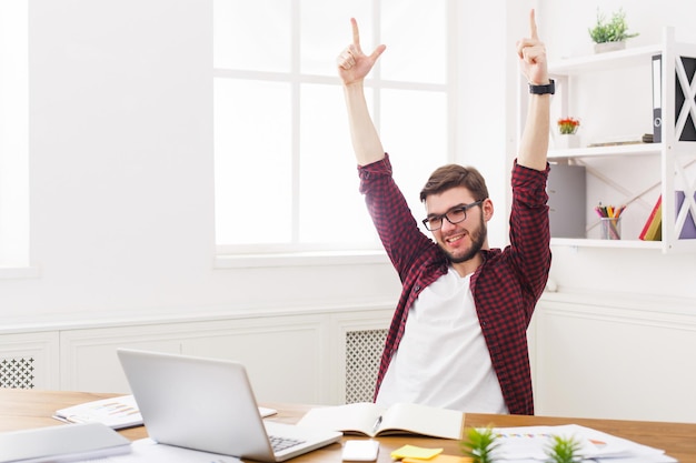 Happy successful businessman win, celebrate in office, sitting at workplace. Man in eye glasses, job in internet.