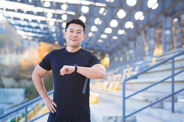 Happy and successful male athlete looks at the camera and smiles Asian happy with the result of his training near the stadium outside in the morning