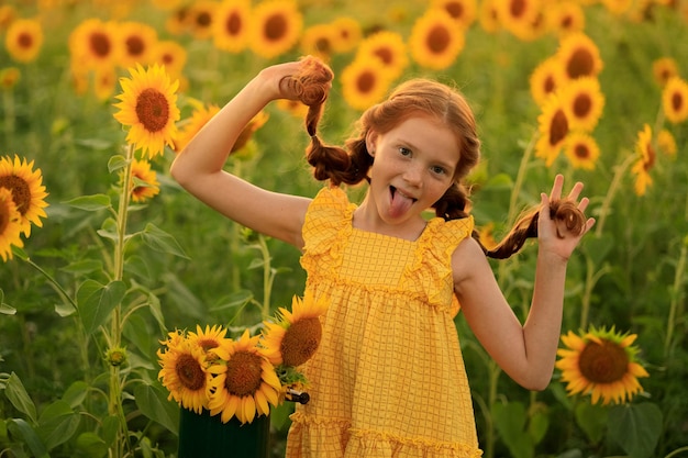 Happy summer in the countryside cheerful redhaired naughty girl with pigtails on a field of sunflowers at sunset