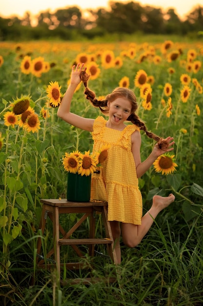 Happy summer in the countryside cheerful redhaired naughty girl with pigtails on a field of sunflowers at sunset