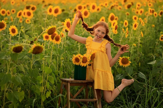 Happy summer in the countryside cheerful redhaired naughty girl with pigtails on a field of sunflowers at sunset