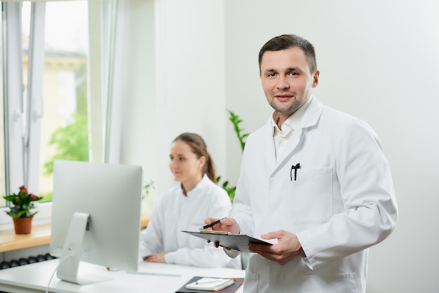 Photo happy surgeon with bristles in a white coat holds a black clipboard smiling