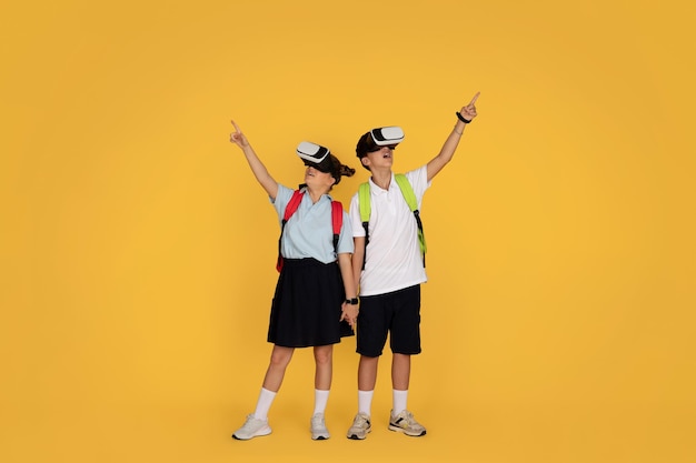 Happy surprised european teen pupil with backpacks in vr glasses point fingers up at free space at