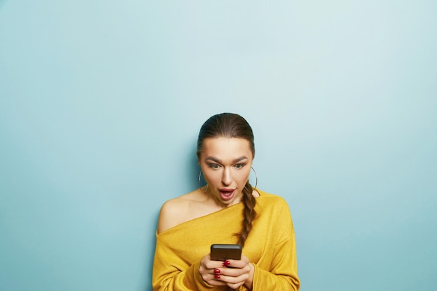 Happy surprised woman uses mobile phone isolated over blue background Mobile communication