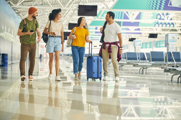 Happy team with luggage talking together while walking on the hall of modern airport