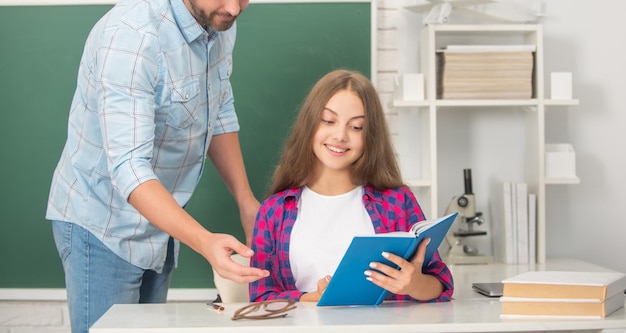 Happy teen girl and cropped teacher man in high school with workbook at blackboard school