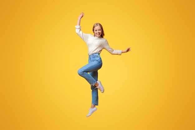 Happy teen girl having fun jumping on orange studio background